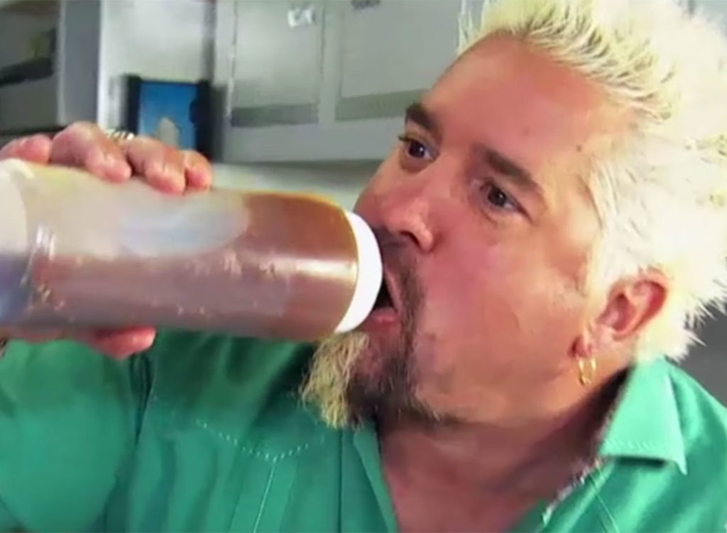 A screenshot from Diners Drive Ins and Dives from the Food Network where Fieri gulps some sort of mystery sauce.