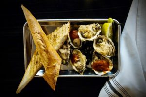 Baked oysters (choice of classic chipotle BBQ, salsa verde, tasso herb) served with lemon & grilled baguette at the Shuckery in Petaluma. (Photo Courtesy: The Shuckery)