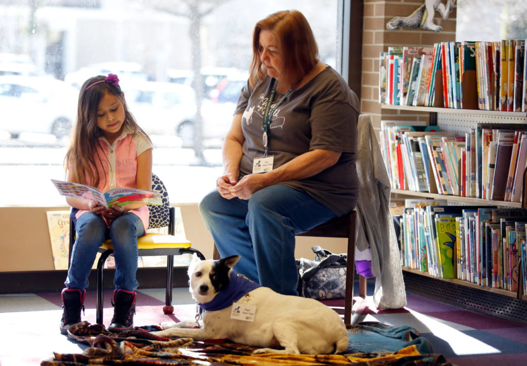 Maggie Hernandez, 7, left, reads aloud to Angel the dog and volunteer Jan Nagy of the Sonoma County Humane Society during the Read to a Dog program at the Central Santa Rosa Library in Santa Rosa, California on Saturday, February 11, 2017. (Alvin Jornada / The Press Democrat)