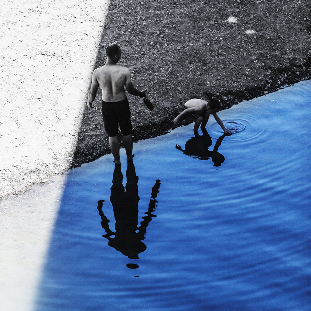 Looking down on a man and a young boy standing in the shaded water along the shore of the Russian River in Monte Rio, California.