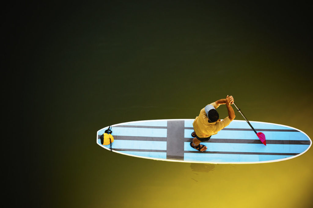 Looking down on a young man standing on his paddle board on the Russian River.