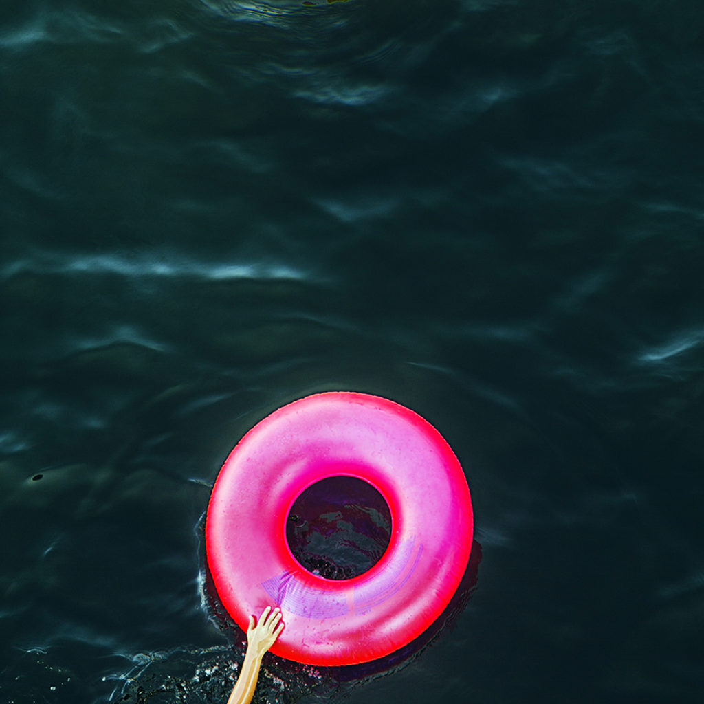 Looking down on a hand reaching out and touching a pink inner tube floating on the Russian River, Monte Rio, California.