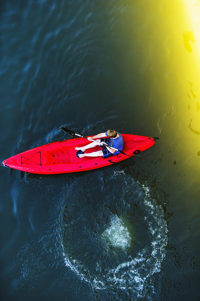 Looking down on a young boy paddling a kayack on the Russian River in Monte Rio, California.