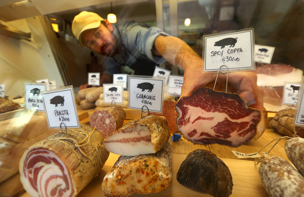 Salumiere Aaron Gilliam reaches for spicy copoa at in the display case at Thistle Meats in Petaluma. (JOHN BURGESS / The Press Democrat)