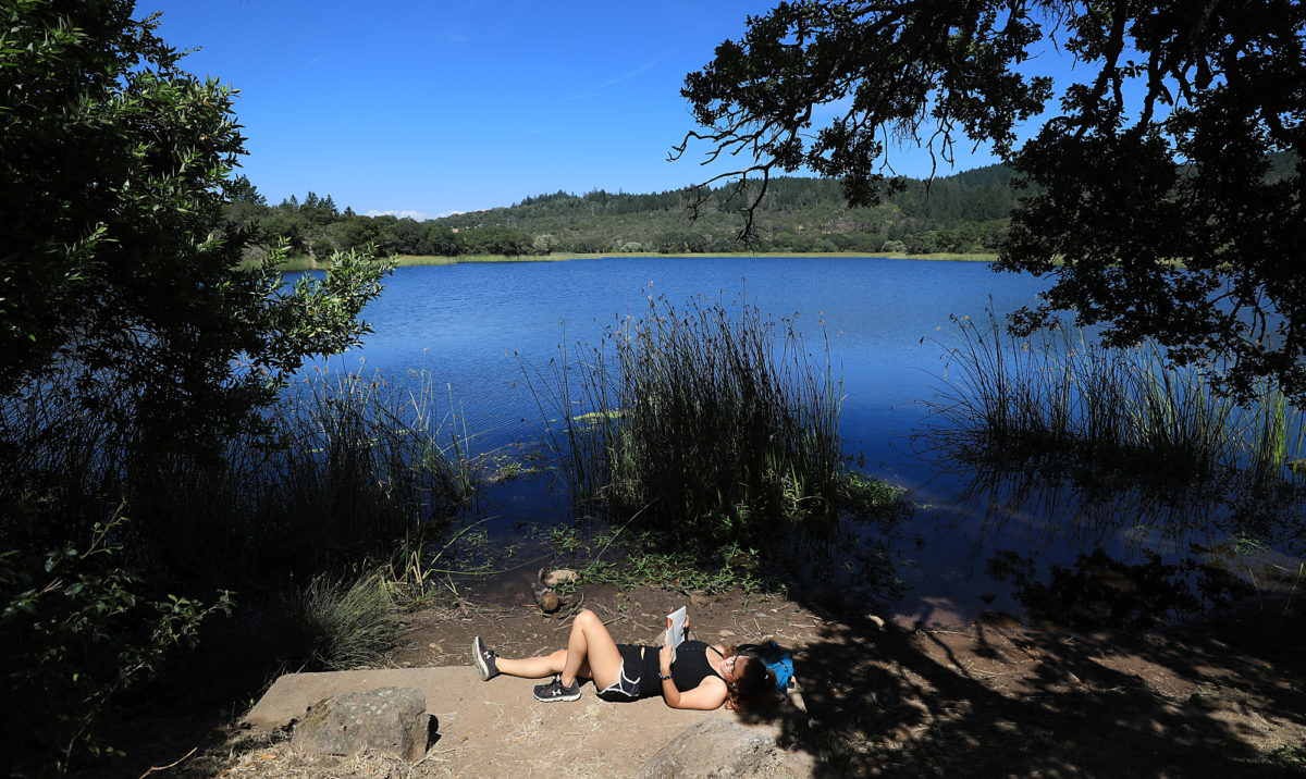Jessie Clarke of Santa Rosa relaxes with a book on the west shore of Lake Ilsanjo in the Trione-Annadel State Park.(Kent Porter/The Press Democrat) 2018