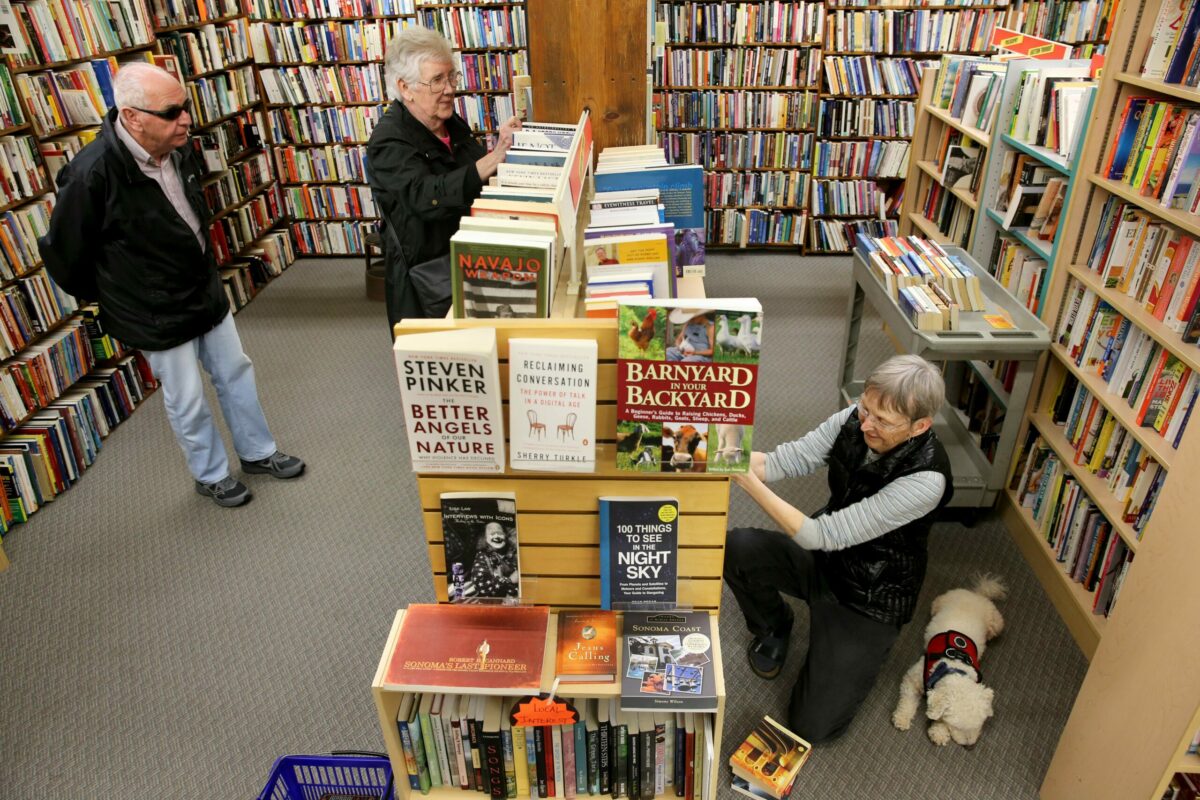 Owner Jill Brown, accompanied by her dog, Marvin, restocks books, as customers Dan and Lyn Jacoby browse through the shelves at Paperbacks Unlimited in Santa Rosa on Monday, April 1, 2019. (Beth Schlanker/ The Press Democrat)