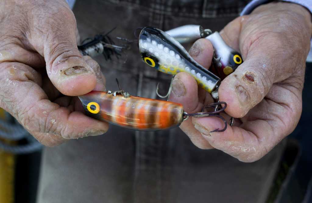 With gnarled hands from years of fishing Dick Ogg shows off the hand painted plugs created by his grandfather when he was a young boy. (John Burgess)