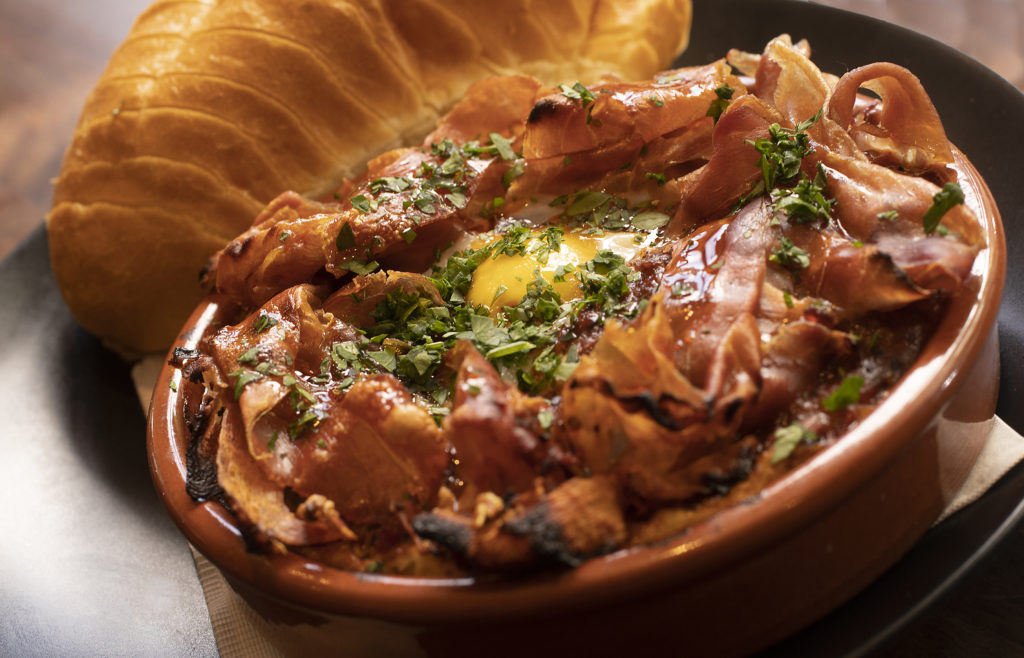 Huevos al Plato with slow-roasted tomatoes, garlic, onions, farm egg and serrano ham with warm baguette from Gerard's Paella Y Tapas in downtown Santa Rosa. (John Burgess)