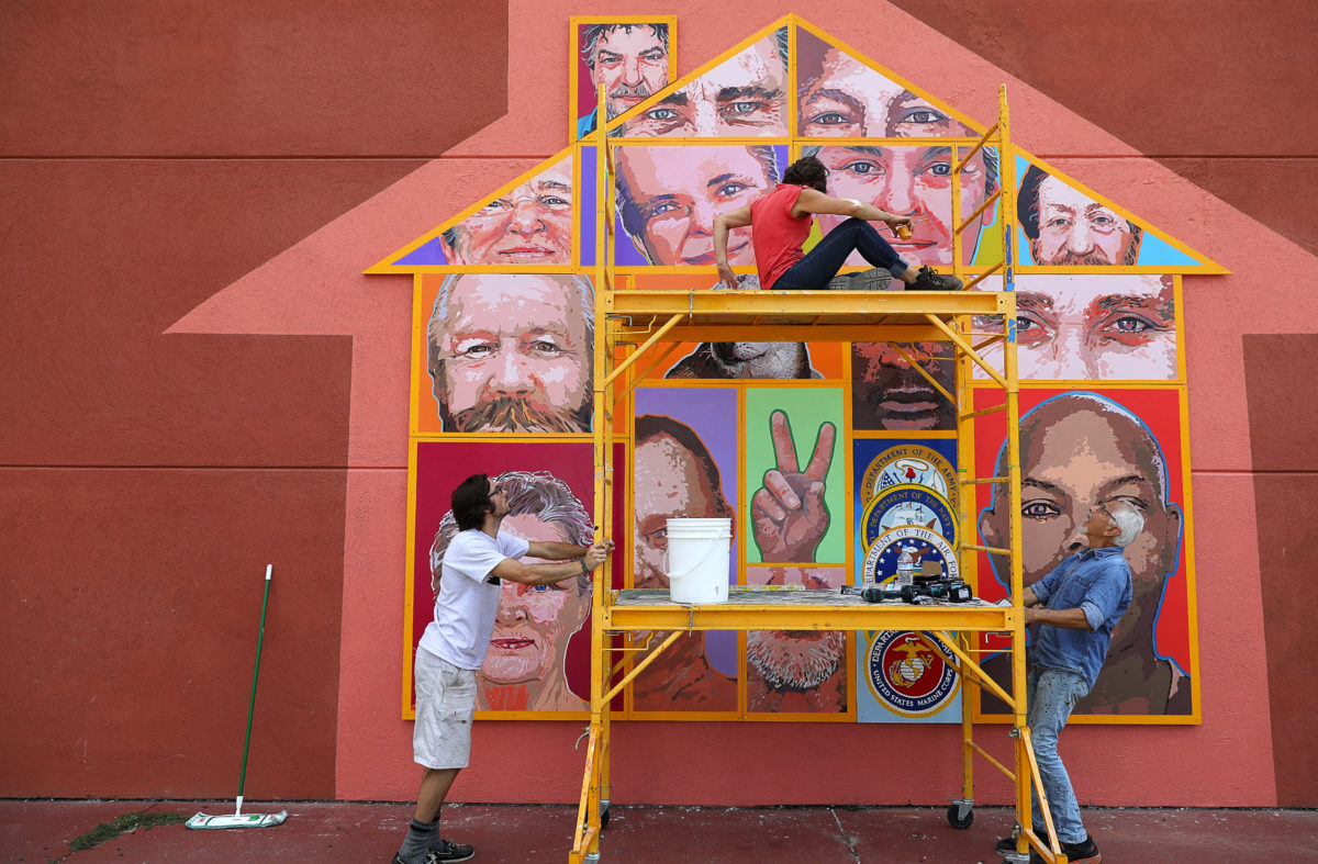 Artists Daniel Doughty, left, and Mario Uribe, right, move a scaffolding holding Jennifer Tatum, so that she can reach another portion of the Palms Inn Project mural, in Santa Rosa on Tuesday, September 12, 2017. The mural is installed on the west side of the Palms Inn, facing Highway 101. (Christopher Chung/ The Press Democrat)