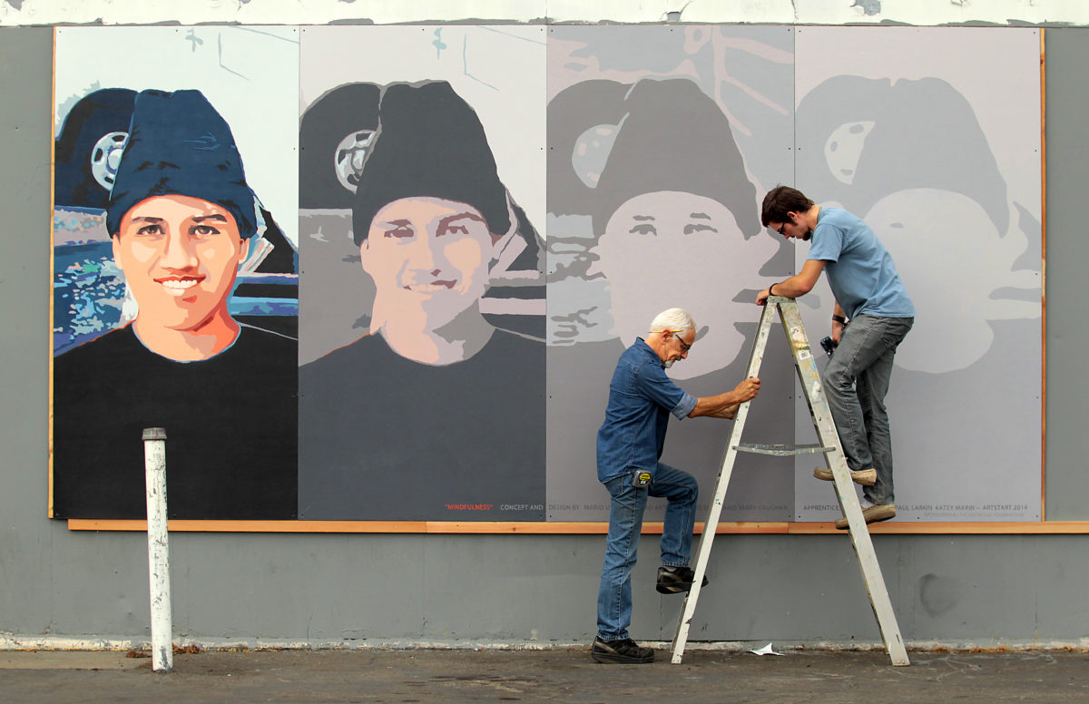 Local artist Mario Uribe, left, holds a ladder for assistant Daniel Doughty as they install a mural in honor of Andy Lopez titled "Mindfulness." The temporary mural was mounted friday morning on a condemned former gas station on West Ave. and Sebastopol Rd.