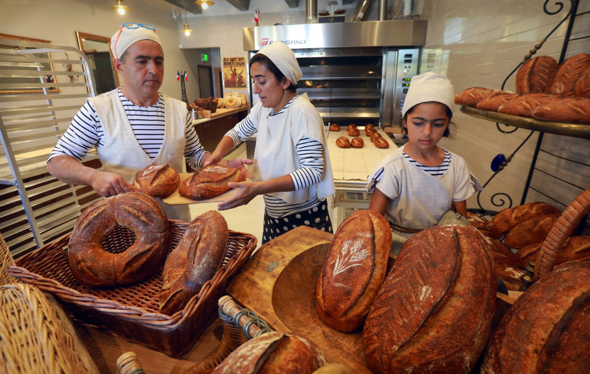 From left, Nas Salamati, his wife Najine Shariat and daughter Soraya Salamati, 11, pulls loves from the oven for display before opening for business at Goguette Bread in Santa Rosa. (John Burgess/The Press Democrat)