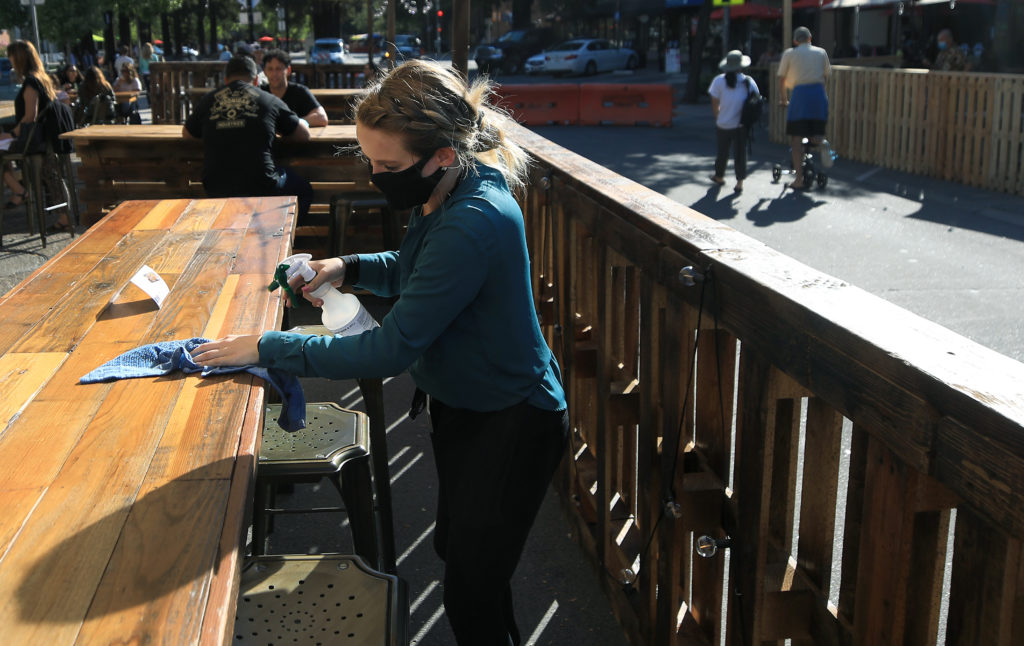 Beer Baron server Emily Gray disinfects an outdoor table along Fourth Street, Friday, July 17, 2020 in downtown Santa Rosa. (Kent Porter / The Press Democrat)
