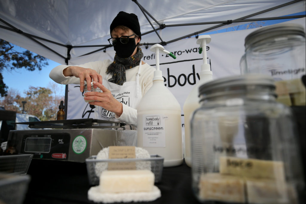 Joan Ayers, owner of Homebody Refill, adds orange essential oil to a mason jar of unscented organic shampoo for a customer at the Petaluma East Side Farmers' Market in Petaluma, Calif., on Tuesday, November 10, 2020. (Beth Schlanker / The Press Democrat)