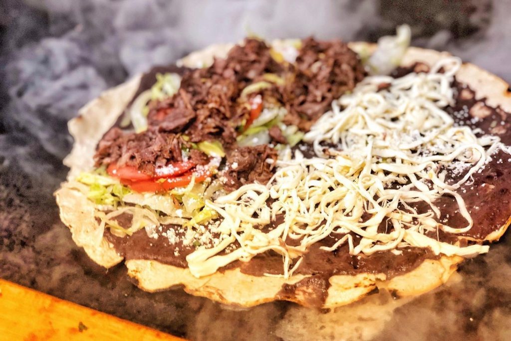 Tlayuda, Oaxacan “pizza” with refried beans, extra layer of lettuce, tomatoes, avocado, quesillo and meat or mushrooms, from Lucha Sabina food truck in Roseland. (Courtesy of Lucha Sabina)