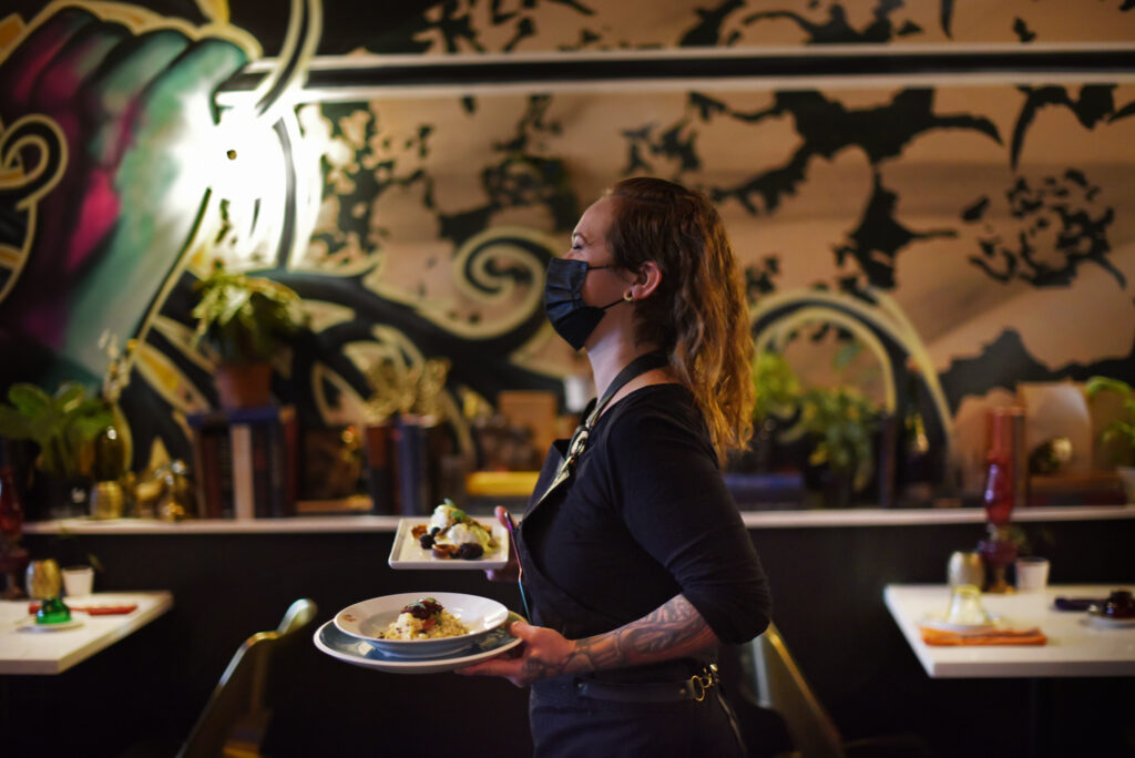 Owner Melissa Matteson delivers a plate of creamed corn risotto and poached eggs served with wild mushrooms and house-cured Liberty Duck prosciutto during a brunch shift at 4th Street Social Club restaurant in downtown Santa Rosa, Calif., on Saturday, Sept. 18, 2021. “Every Wednesday we go foraging,” said Matteson, who is proud that they source all their food within a 40-mile radius of the restaurant. (Erik Castro / For The Press Democrat)