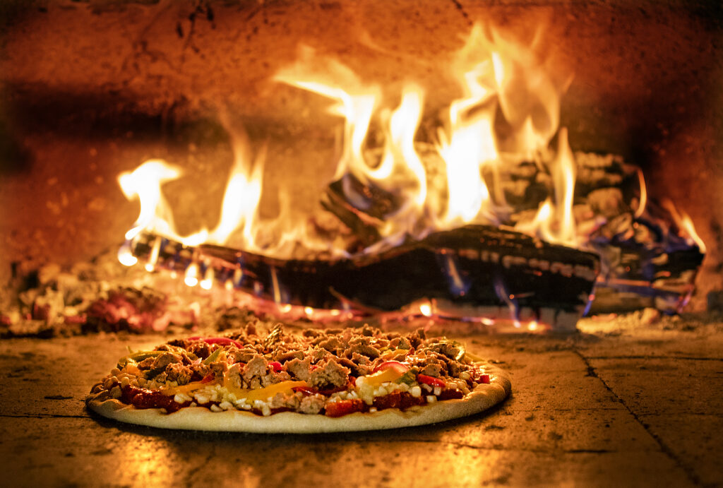 A Peppers and Sweet Italian Sausage Pizza with mozzarella and bitter greens cooks in the wood oven at The Mill at Glen Ellen. (John Burgess/The Press Democrat)