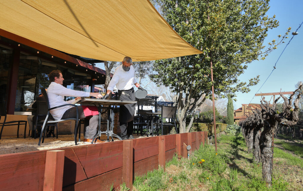 Alan Luzmoor, right, serves a glass of wine to Duncan Lish at the John Ash & Co restaurant in Santa Rosa. (Christopher Chung/ The Press Democrat)