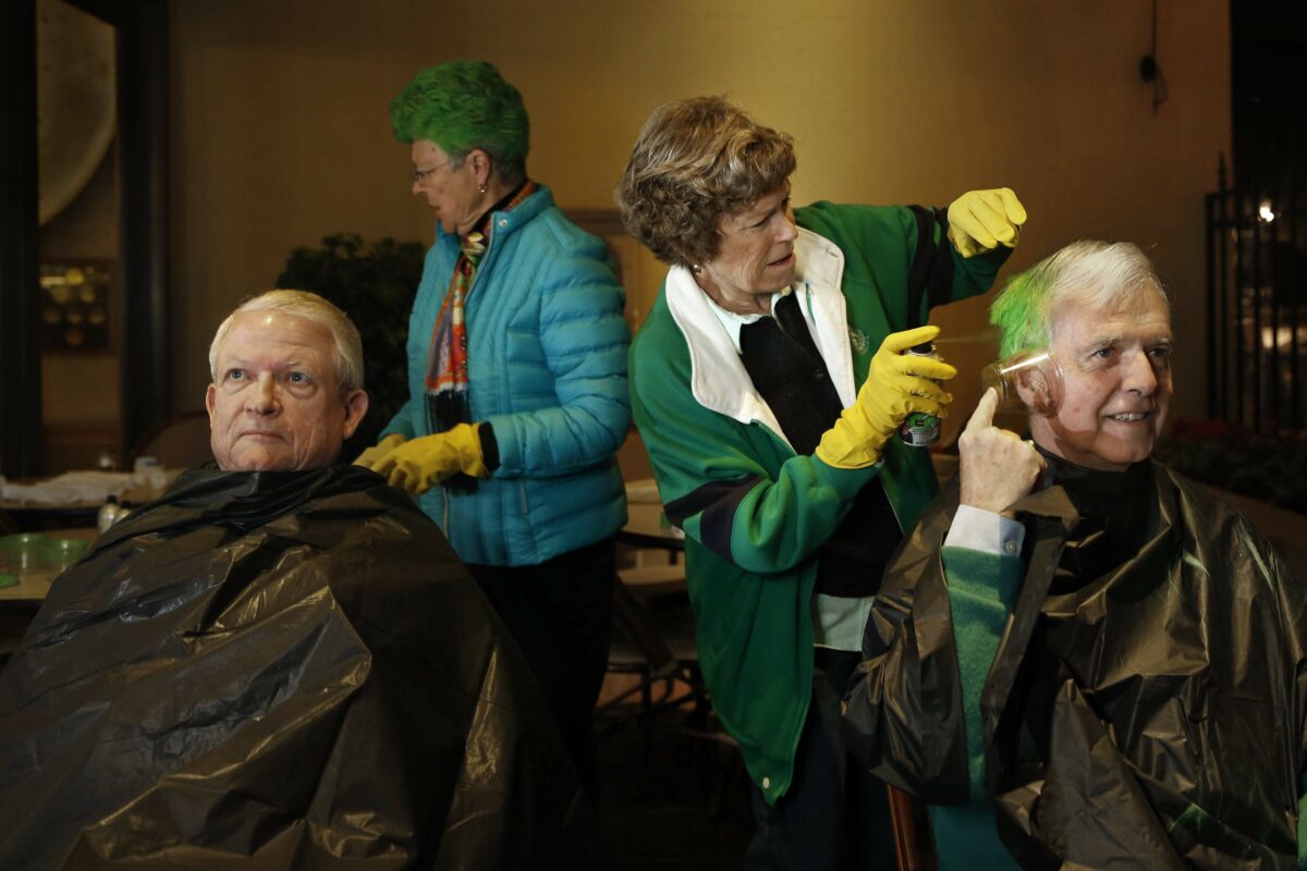 David Anderson, right, uses a cup to cover his ear as his wife, Cathy, spray paints his hair green. Wally Schultz, left, waits for Lynda Guthrie to paint his hair before the start of the St. Patrick's Day parade in Healdsburg, on Tuesday, March 17, 2015. (Beth Schlanker/The Press Democrat)