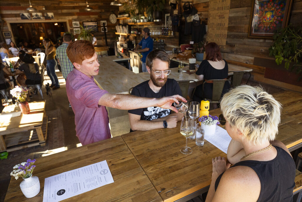 Charlie Moore, left, serves wine to guests sitting the Pax Winery tasting room bar window at The Barlow in Sebastopol. (John Burgess/Sonoma Magazine)