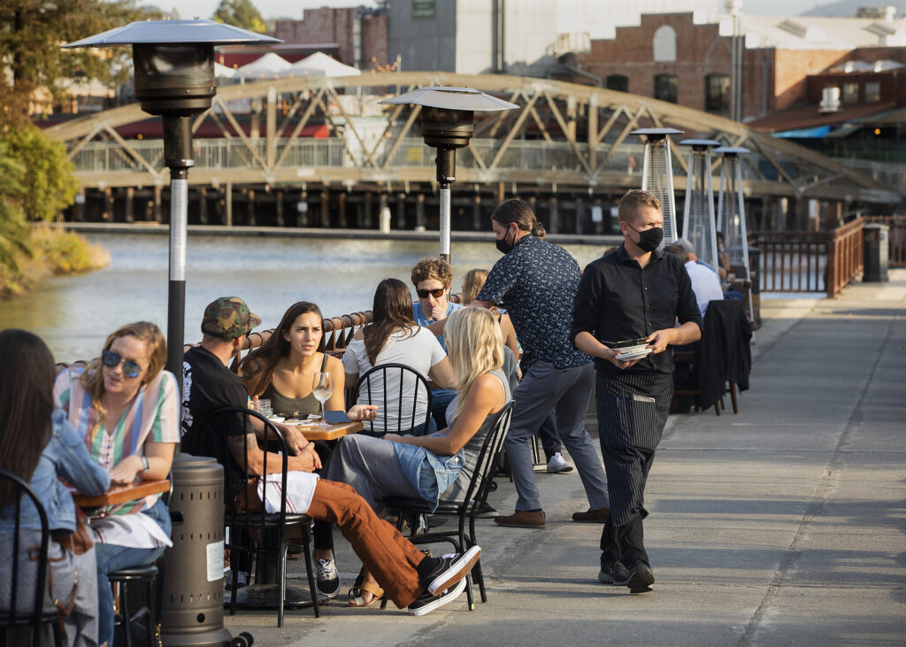Diners enjoy the newly expanded newly expanded seating area along the Petaluma river at Seared, foregrounded, and Risibisi restaurants in downtown Petaluma on Friday, September 18, 2020. Cucina Paradiso & Central Market restaurants also expanded their seating. (Photo by John Burgess/The Press Democrat)