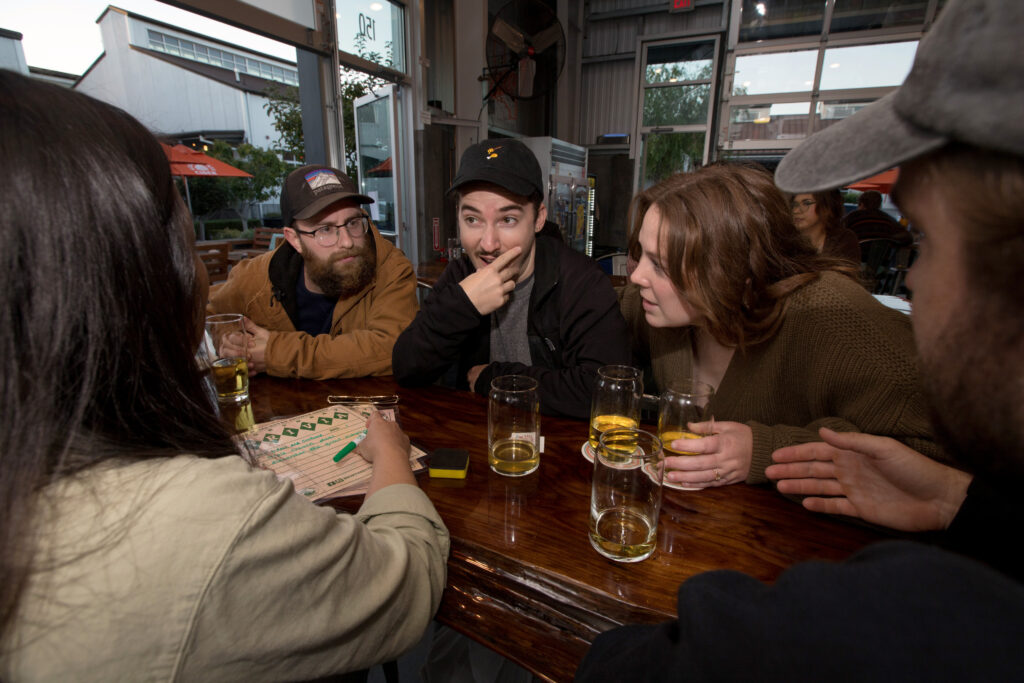 Left to right (center), Tanner Faber, Michael Estens, and Katie-Lauren Dunbar (hyphenated first name), along with Lauren Hemmingsen and Eric Kroh (backs to camera), all of Santa Rosa, calling themselves the team name "Bidets and Confused" discuss their answers to trivia questions during trivia night presented by North Bay Trivia at Golden State Cider Taproom, Thursday, October 13, 2022, in Sebastopol. (Darryl Bush / For The Press Democrat)
