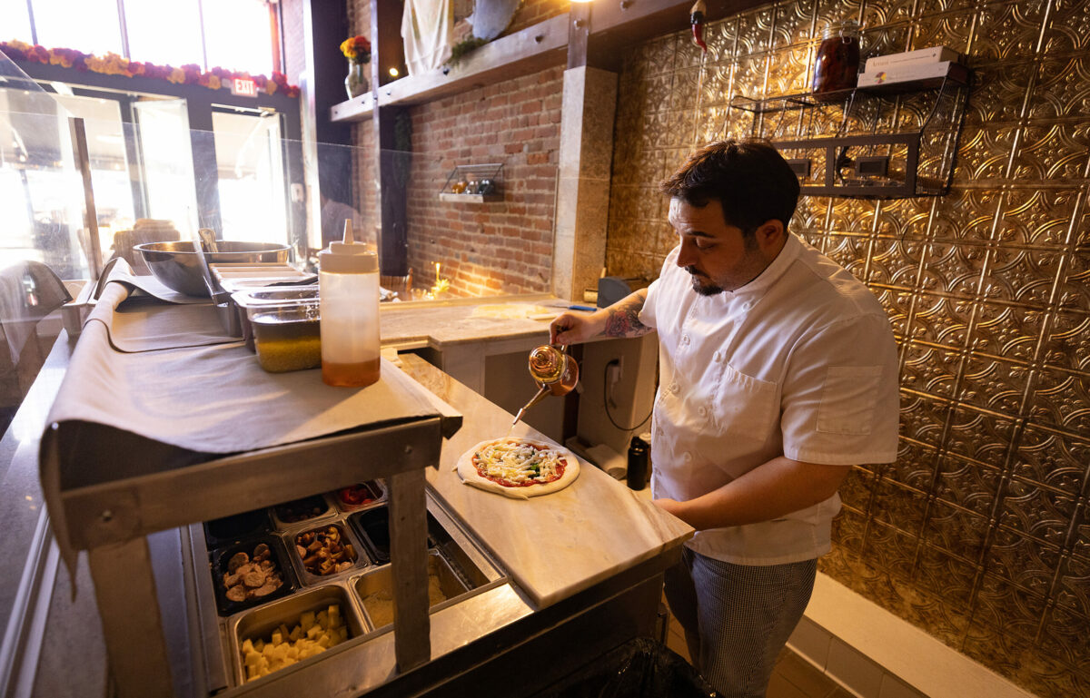 L'Oro di Napoli owner Domenico De Angelis adds a drizzle of olive oil to a pizza in downtown Santa Rosa March 24, 2023. (John Burgess/The Press Democrat)