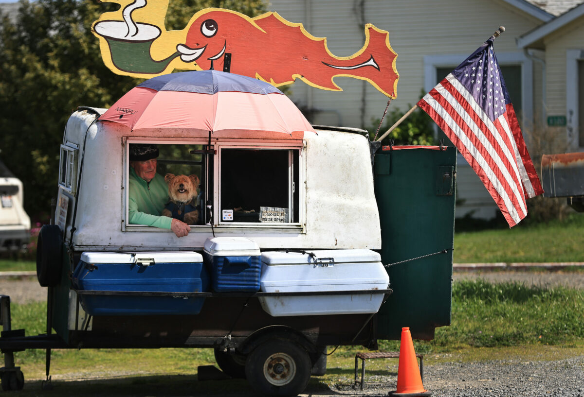 Greg Brummet and his dog Bungee wait patiently for a customer to pull up and buy smoked salmon at Brummet's usual spot on Highway 12 just west of Sebastopol, Friday, March 17, 2023. (Kent Porter / The Press Democrat) 2023