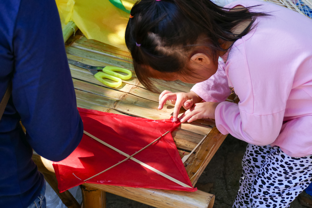 The people teach their children to make paper kite on the bamboo table.