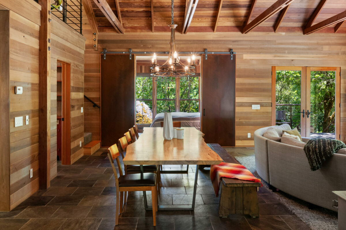 The dining area of the great room enjoys forest views on all sides thanks to large cedar-framed windows and doors. (Lunghi Studios)