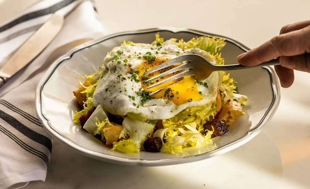 Salade Lyonnaise with frisée, curly chicory, bacon vinaigrette, lardons, croutons and sunny side egg from Augie’s French Tuesday, November 28, 2023, on Courthouse Square in Santa Rosa. (John Burgess/The Press Democrat)