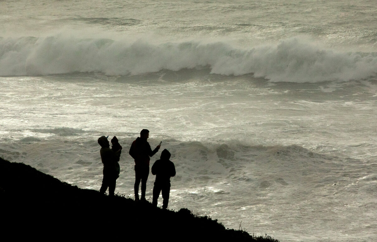 A family took the opportunity during a break in the rain to watch the giant waves crash high up on the Sonoma Coast at Schoolhouse Beach Friday, January 13, 2023. (John Burgess/The Press Democrat)