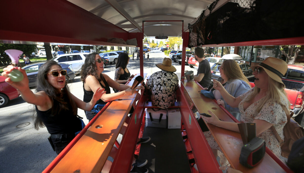 Pedaling around the Healdsburg Plaza, at left, Julie Mendoza of Walnut Creek, Christina Dudley of Pacifica and Monica Becker of Hollister join Lisa Fowler of Redwood City, in blue, and Katie Farah, in hat, for a bachelorette party for bride to be Erica Morales of Hayward, out of the frame at right, aboard Bike Healdsburg.com. The driver is Tim Buckner, middle with co owner Chris Pilling, Saturday, April 10, 2021. Co owner Jessica Pilling says the pandemic closed their business down for near 3/4 of the year, which said was "Brutal". As the economy begins to open up, their bookings have increased. (Kent Porter / The Press Democrat) 2021