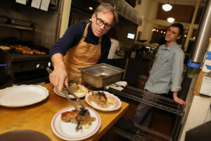 Chef Mark Malicki prepares plates of Stemple creek meatloaf, duck fat fried potatoes, black chanterelle butter bath & greens, while Jack Reed waits to serve them to customers, at de Havilland in Petaluma on Friday, January 12, 2024. (Christopher Chung/The Press Democrat)