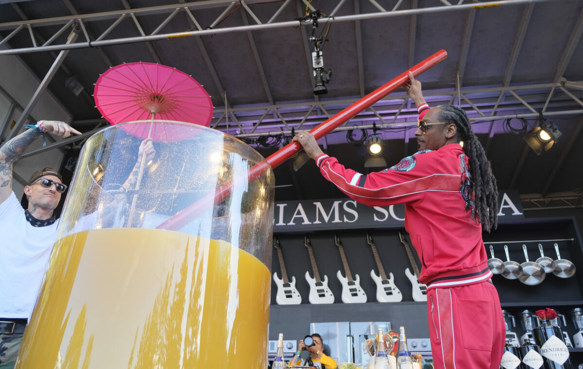 In this photo taken Saturday, May 26, 2018, Snoop Dogg, right, stirs the world's largest paradise cocktail after adding gin to it on a culinary stage at the BottleRock Napa Valley music festival in Napa, Calif. A Guinness World Records official was on hand to certify the record of the 550 liter cocktail. Looking on at left is Top Chef Michael Voltaggio. (AP Photo/Eric Risberg)