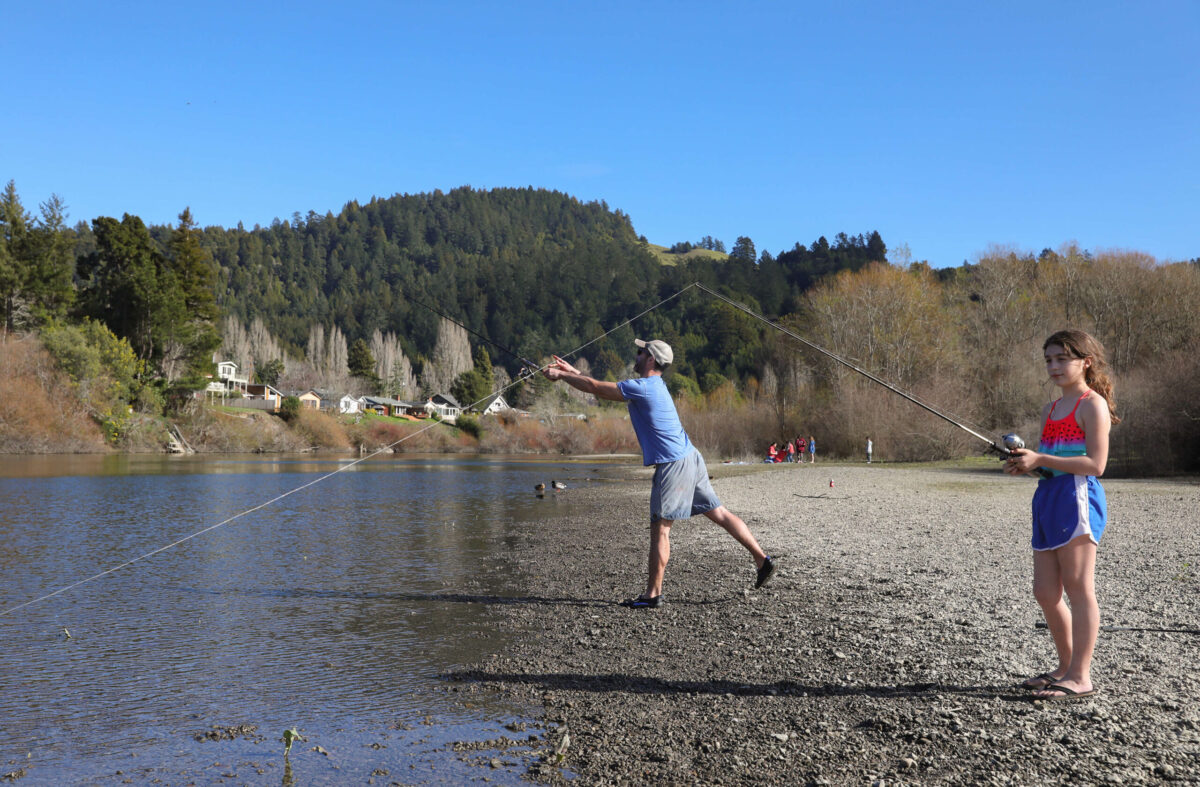 Tom Schmidt, of Novato, fishes with his daughter, Isabella, 10, on the beach at Casini Ranch Family Campground, along the Russian River, in Duncans Mills on Wednesday, February 17, 2021. (Christopher Chung / The Press Democrat)