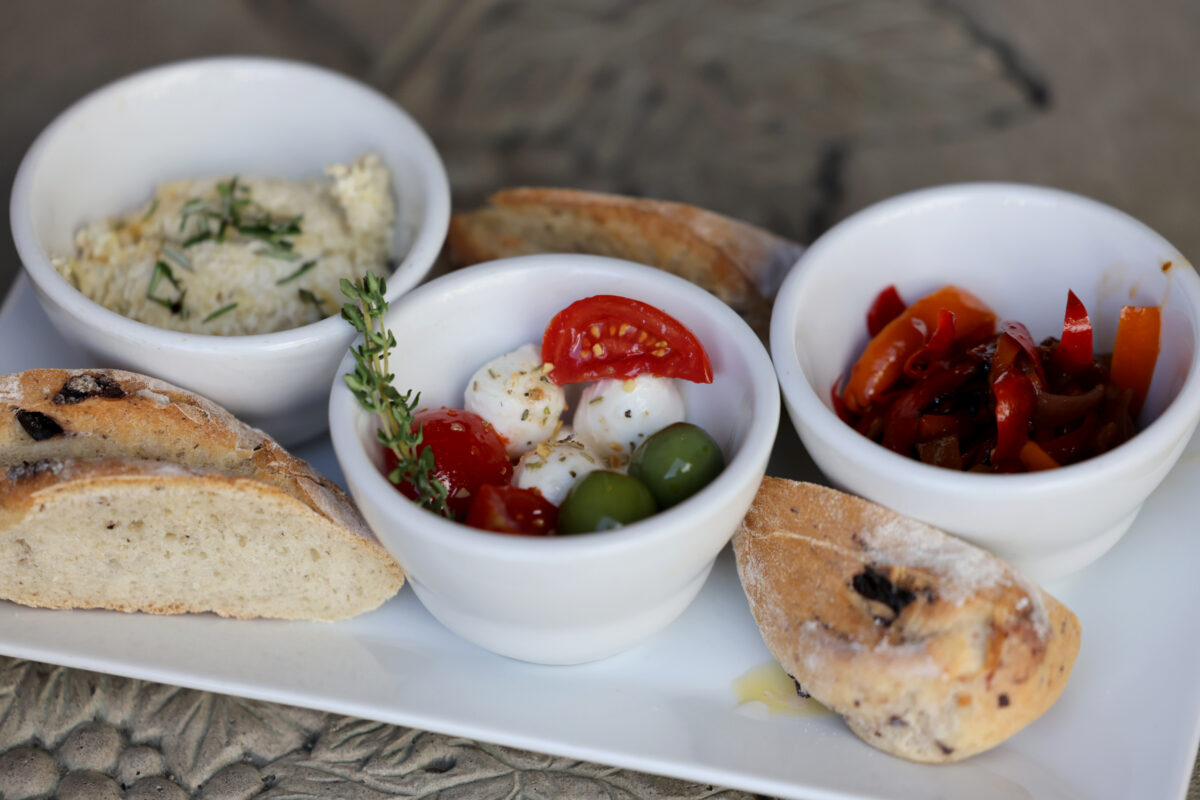 A trio of appetizers including baked artichoke dip, mozzarella and marinated tomatoes, and sweet and sour peppers and onions, served with housemaid bread at Portico in Sebastopol, Wednesday, April 24, 2024. (Beth Schlanker / The Press Democrat)