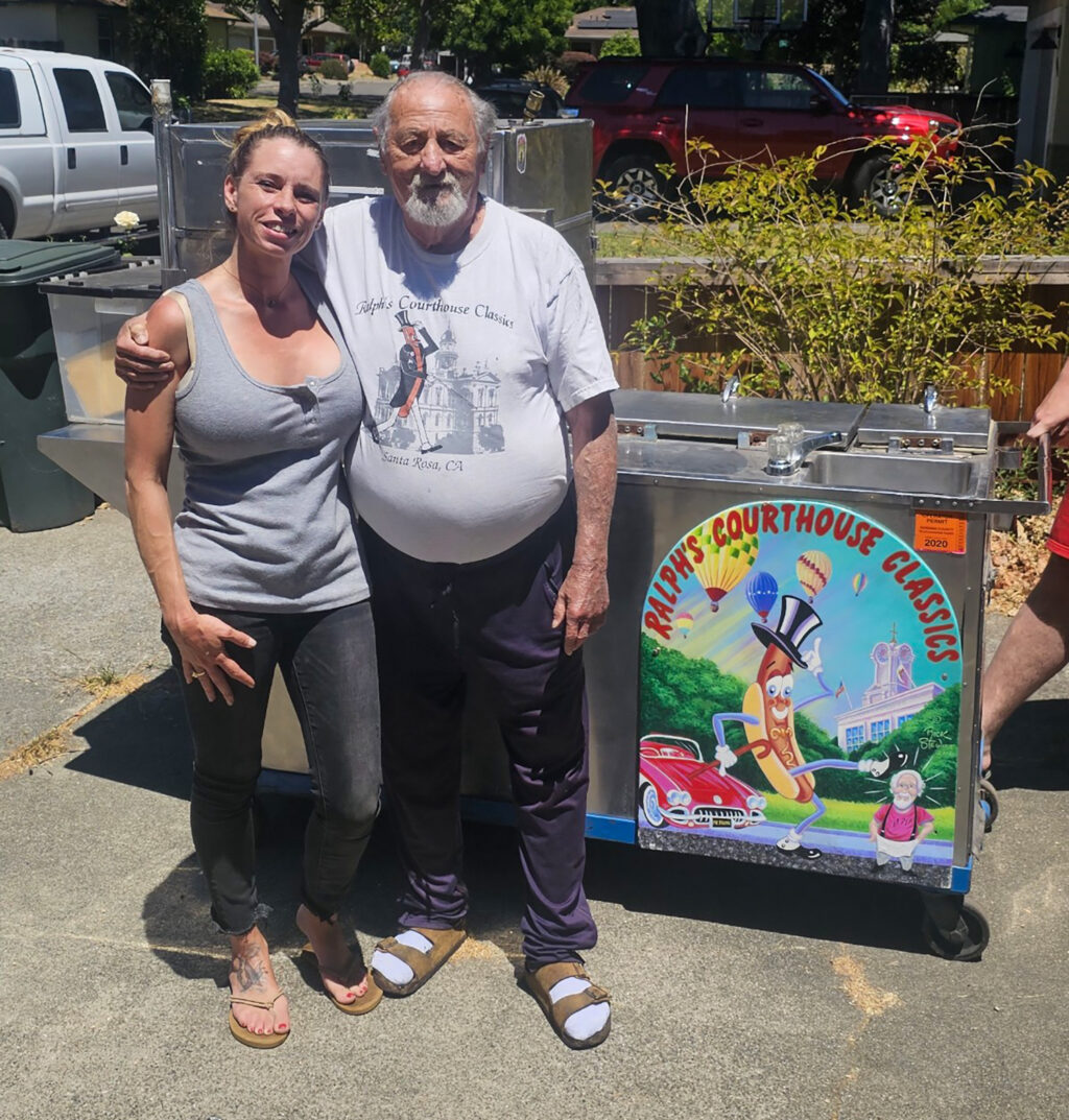 Ralph Morgenbesser of Ralph's Courthouse Classics hot dogs and Milli Cannata of SLYC Kidz pose in front of the iconic cart that he donated. (Photo: Milli Cannata)