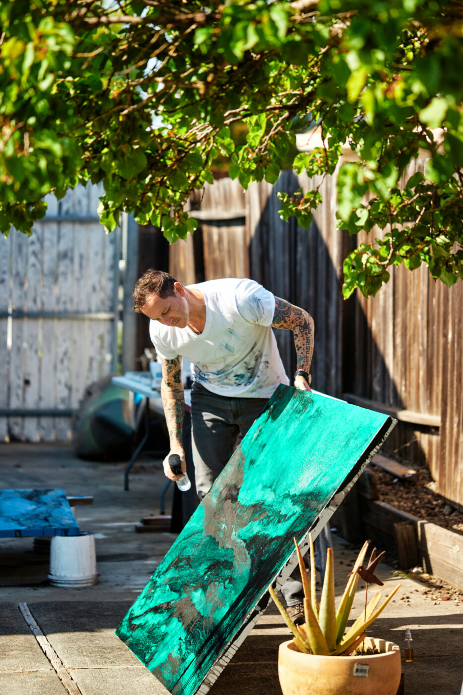 Recently back from deployment, artist Aaron Webb works in the side yard of his Petaluma home. He creates texture by scraping the paint, spraying the canvas with alcohol, rubbing the surface with dirt or salt — even leaving the painting outdoors overnight so drizzle and fog can apply a final glowing coat. (Kim Carroll/for Sonoma Magazine)