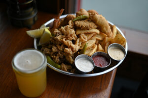 A cold beer with the Captain’s Platter served with Dungeness crab, fried calamari, beer battered shrimp and rock cod with a side of Dipper fries at Rocker Oysterfeller’s at Lucas Wharf in Bodega Bay on Friday, Aug. 23, 2024. (Erik Castro / For The Press Democrat)