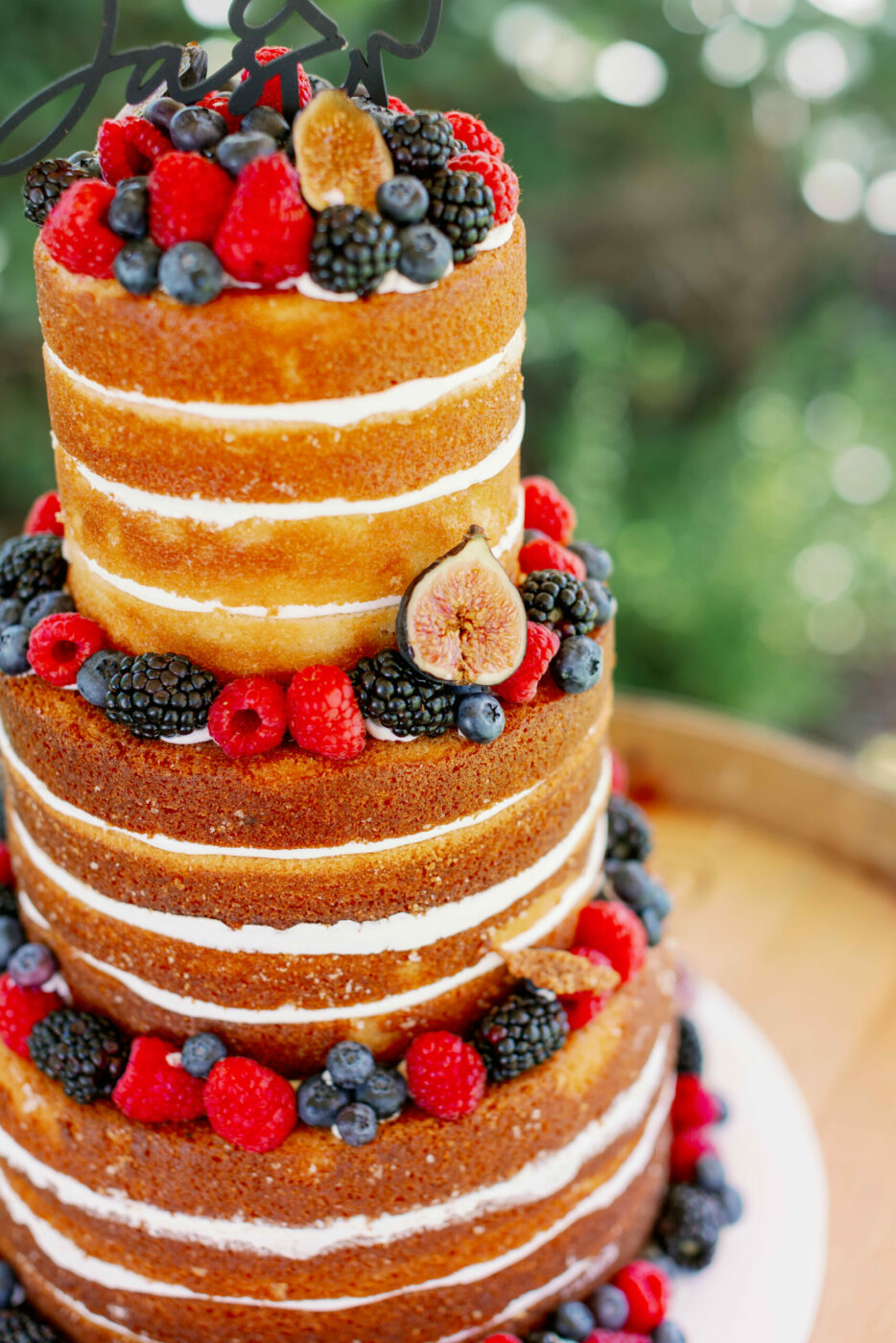 A multi-tiered wedding cake topped with fresh berries and figs by Flour and Bloom Cakes. (Kathryn White)