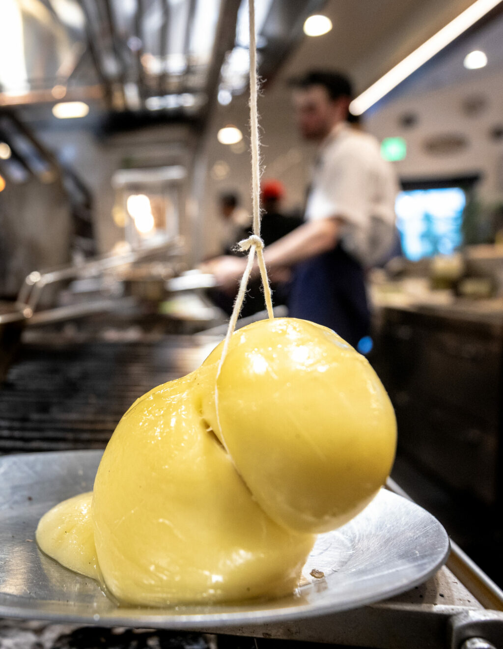 Melting mozzarella imported from Puglia, Italy hangs next to the open grill for the Scamorza Impiccato appetizer at Stella Wednesday, March 26, 2025, in Kenwood. (John Burgess / The Press Democrat)