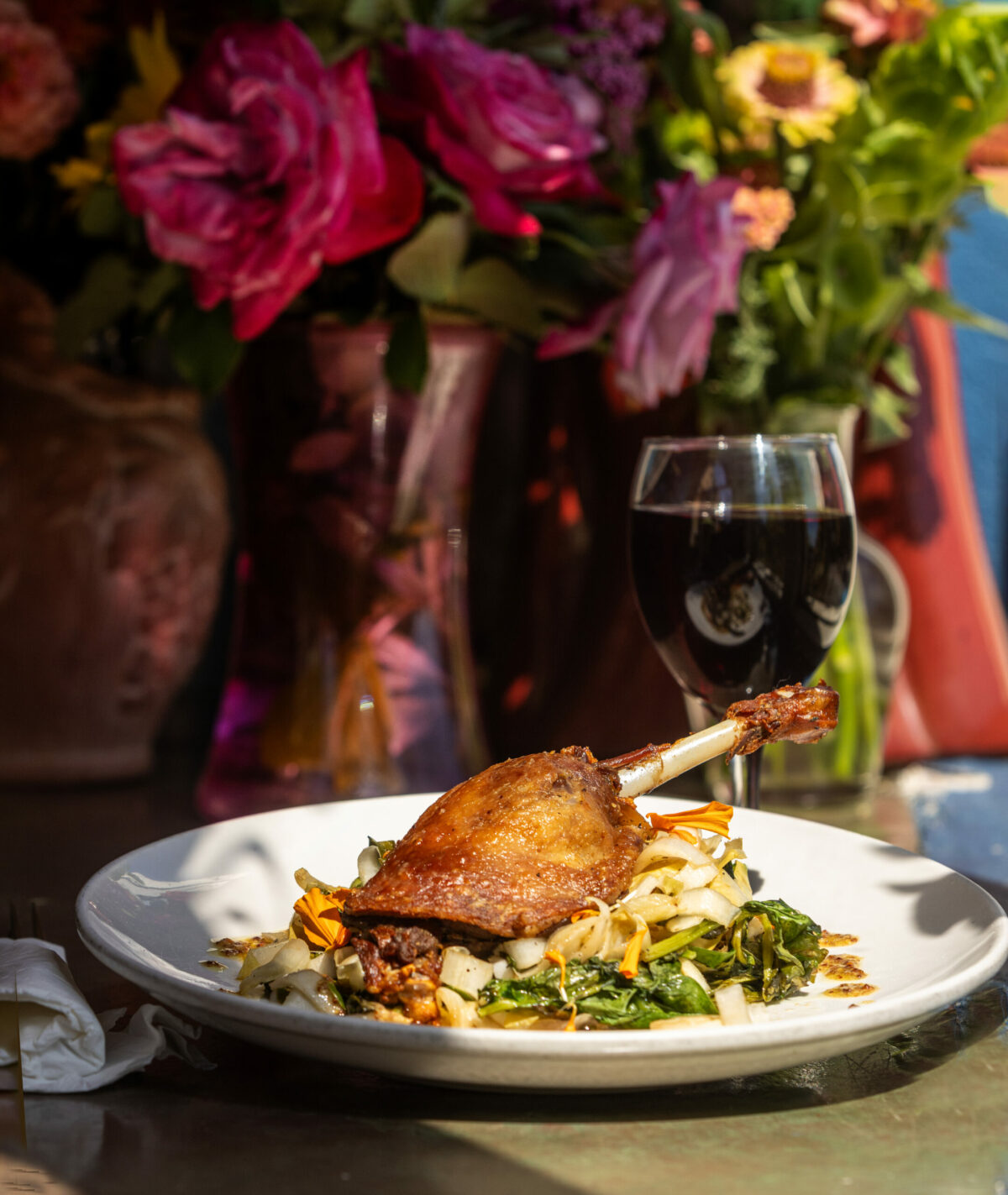 Duck Confit with endive and spinach and a glass of wine in a sunny window seat at Water Street Bistro Thursday, August 29, 2025 in Petaluma. (John Burgess / The Press Democrat)