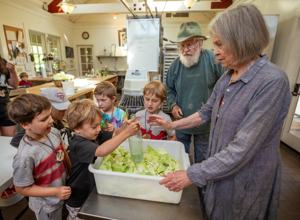 Susan, right, and Lou Preston demonstrate how to use a bottle to mash cabbage when making sauerkraut during the LandPaths Owl camp at Preston Farm in the Dry Creek Valley in spring 2019. (John Burgess / The Press Democrat)