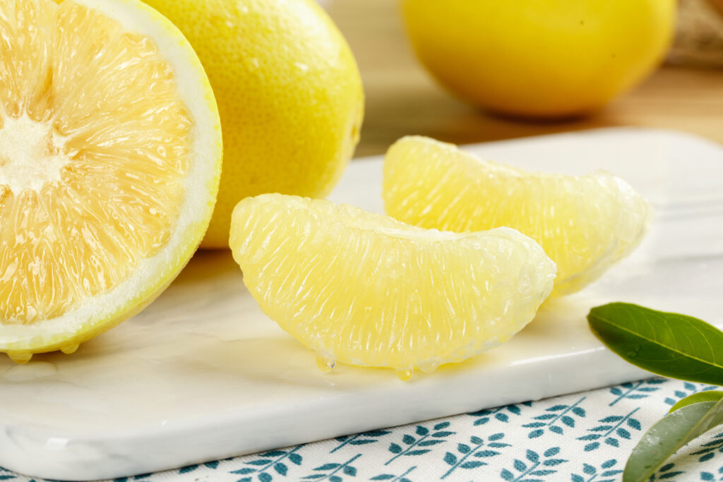 Fresh peeled pomelo segments and halved grapefruit on white plate, showcasing juicy citrus fruit texture and natural sweetness from Fujian region. (Truong Hoang Tuan / Getty Images)