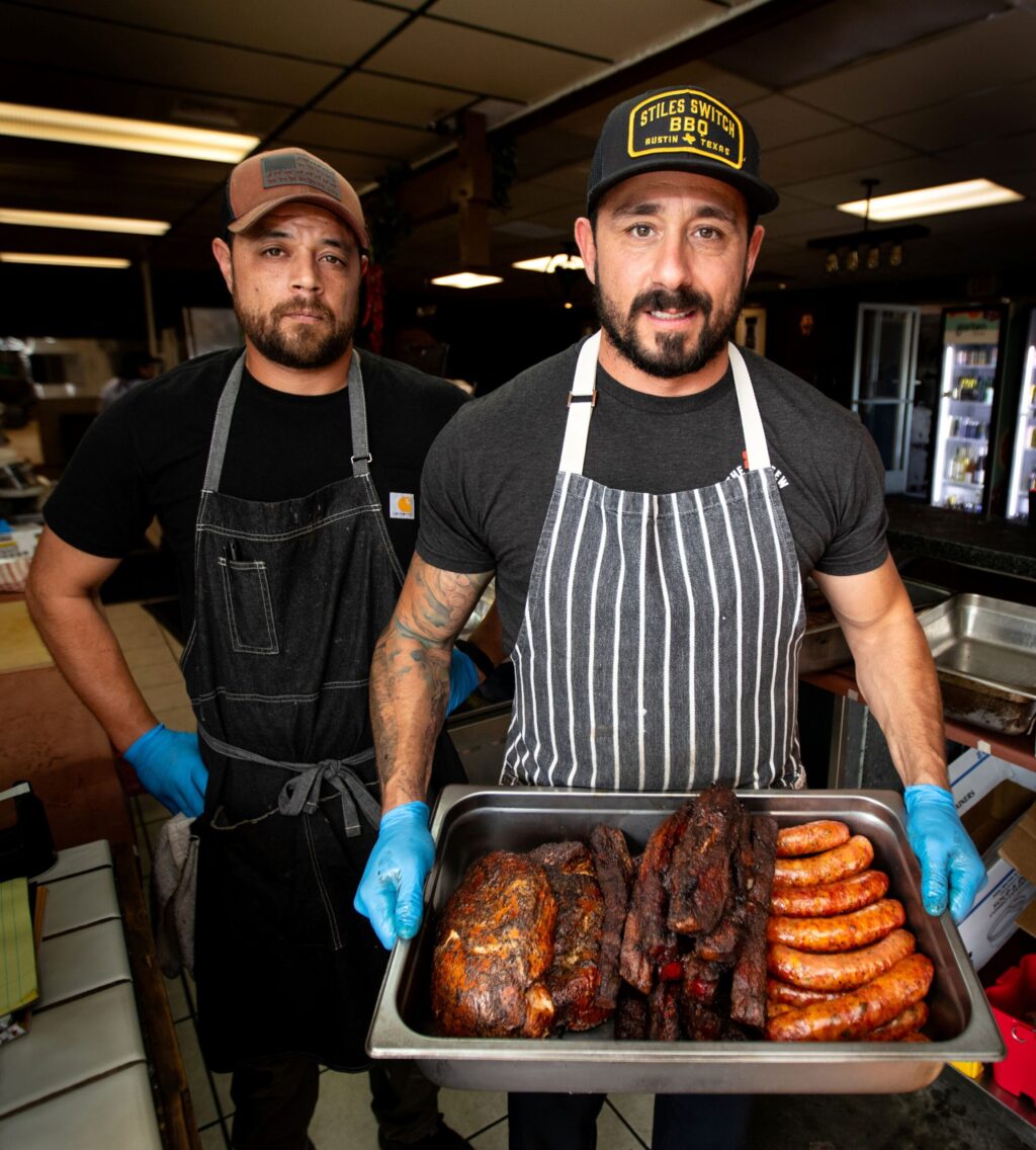 Bob Costarella, owner and pitmaster, holds a pan of barbecued meats next to, Brendon Welcker, sous chef, as they prepare to sell food at his “Red Eye Barbecue” pop-up, held on Saturdays at Sazon Peruvian Cuisine & Deli on Nov. 15, 2025. (Darryl Bush / For The Press Democrat)