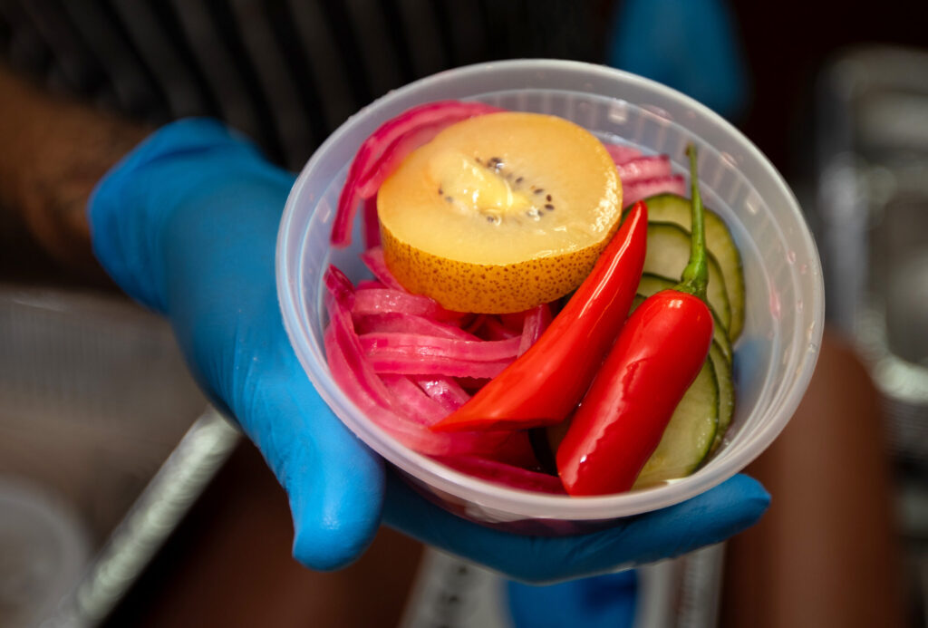 Bob Costarella, owner and pitmaster, holds a side of pickled veggies and fruits at his “Red Eye Barbecue” pop-up, held on Saturdays at Sazon Peruvian Cuisine & Deli on November 15, 2025. (Darryl Bush / For The Press Democrat)
