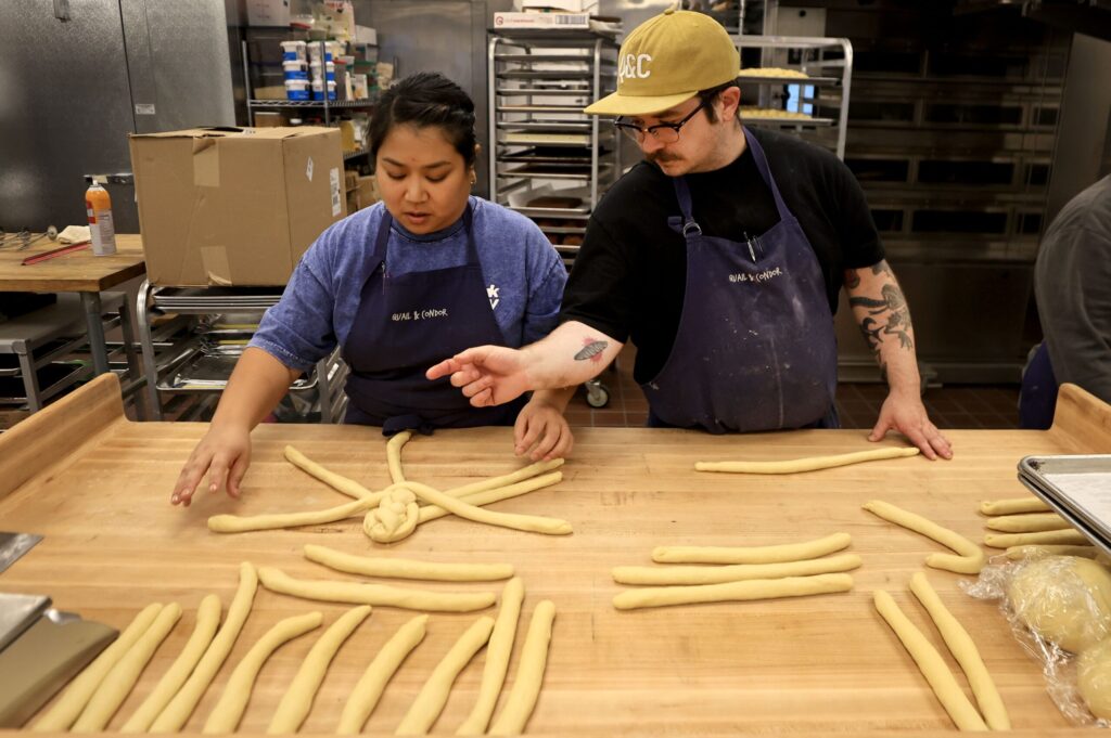 Alex Fong teaches Thida Vattanawase the finer points of braiding Challah bread at Quail & Condor in Healdsburg, Thursday, Nov. 20, 2025. (Kent Porter / The Press Democrat)
