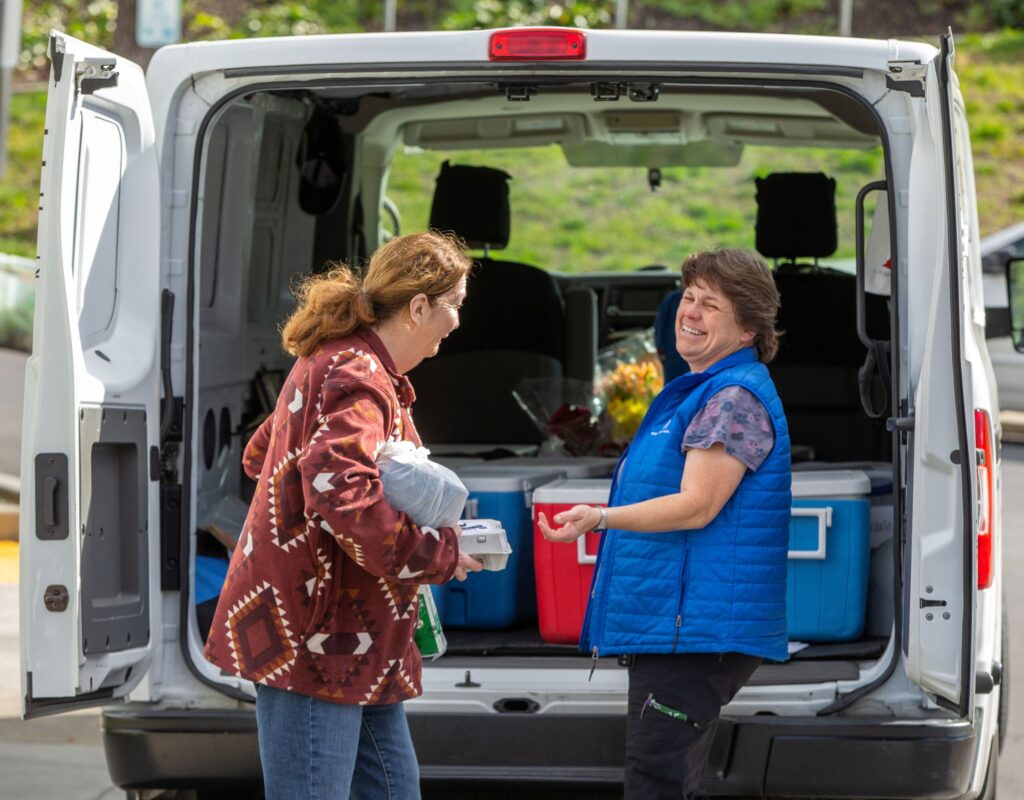 Longtime Council on Aging Meals on Wheels driver and Fleet Manager Shannon Holck smiles after handing off a meal at the Drive Up/Pick Up site in front of the senior center at King's Valley Senior Apartments in Cloverdale, February 21, 2023. (Chad Surmick / The Press Democrat)