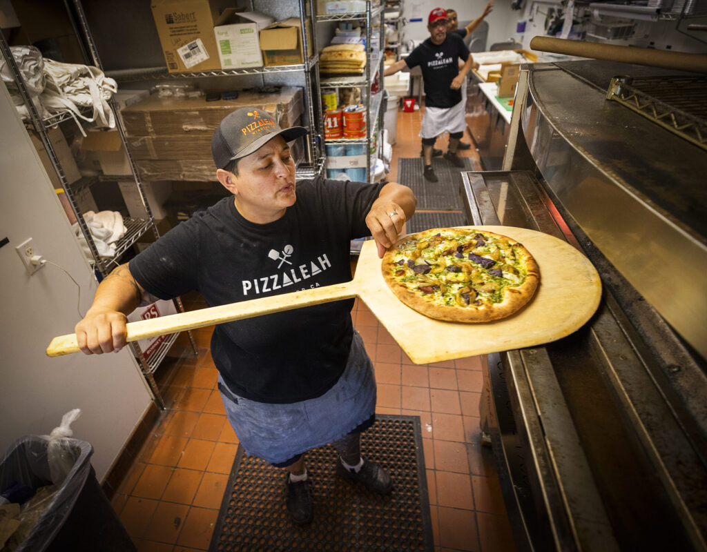 Leah Scurto, owner of PizzaLeah, checks to see if a pizza crust its crisp enough to serve at her Windsor restaurant. (John Burgess/The Press Democrat)
