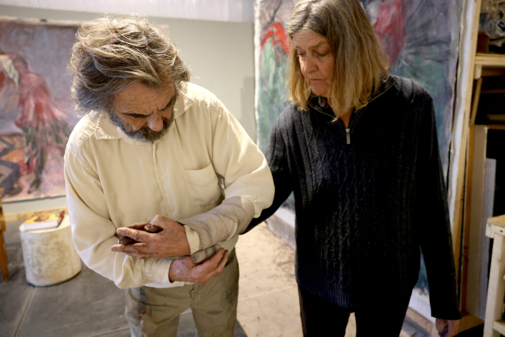 Artists Pamela Holmes and Winston Gourley bind their arms together before working on a painting at Stranger Worth studio in Cazadero Thursday, Nov. 20, 2025. (Beth Schlanker / The Press Democrat)